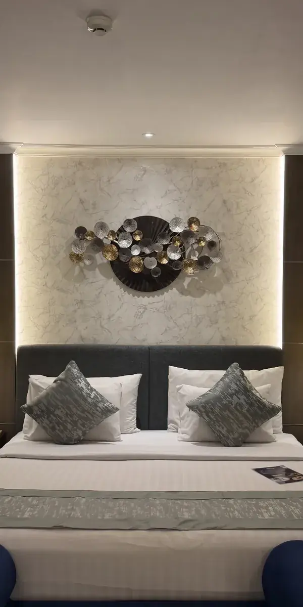 Headboard kamar hotel dengan backdrop HPL motif marmer putih diapit panel kayu gelap dan lampu gantung